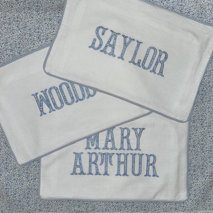 Three white pillow covers with embroidered names on a textured surface