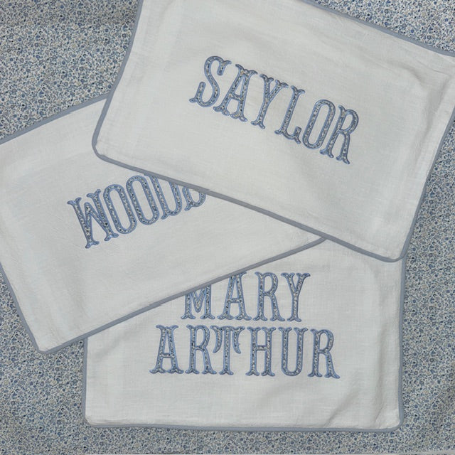 Three white pillow covers with embroidered names on a textured surface