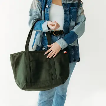 Person holding a green tote bag against a white background