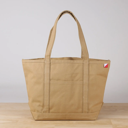 Tan tote bag with a small red and white logo on a light gray background