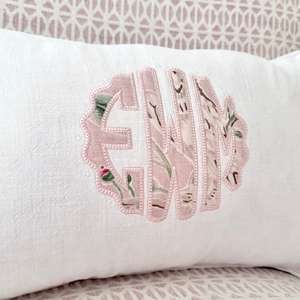 White pillow with floral embroidered initials on a patterned background